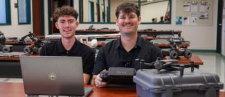 Two male PHSC aviation students sitting next to a drone.