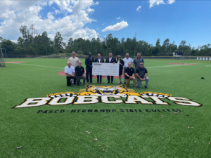 PHSC and WREC representatives holding large check standing on Bobcats logo on baseball field 